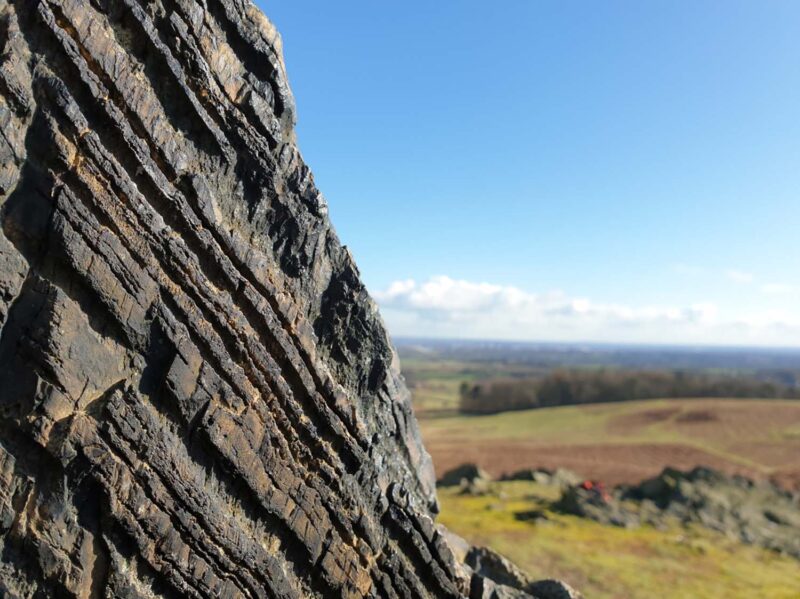 Included centimetre thick layers of rock, with out of focus green landscape in the background.